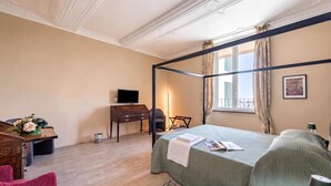 A four-poster bed with a green bedspread, a desk with a computer, a chair, and a small table with flowers. - Precious House Genova Porto Antico (Genoa)
