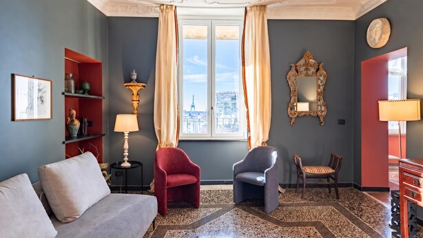 A room with a sofa, two chairs, a decorative lamp, a mirror, and a view of a cityscape through a window. - Precious House Genova Porto Antico (Genoa)