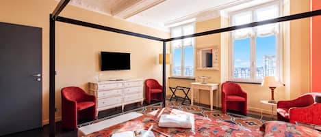 A four-poster bed with a floral bedspread, a television on a dresser, and a city view through large windows.