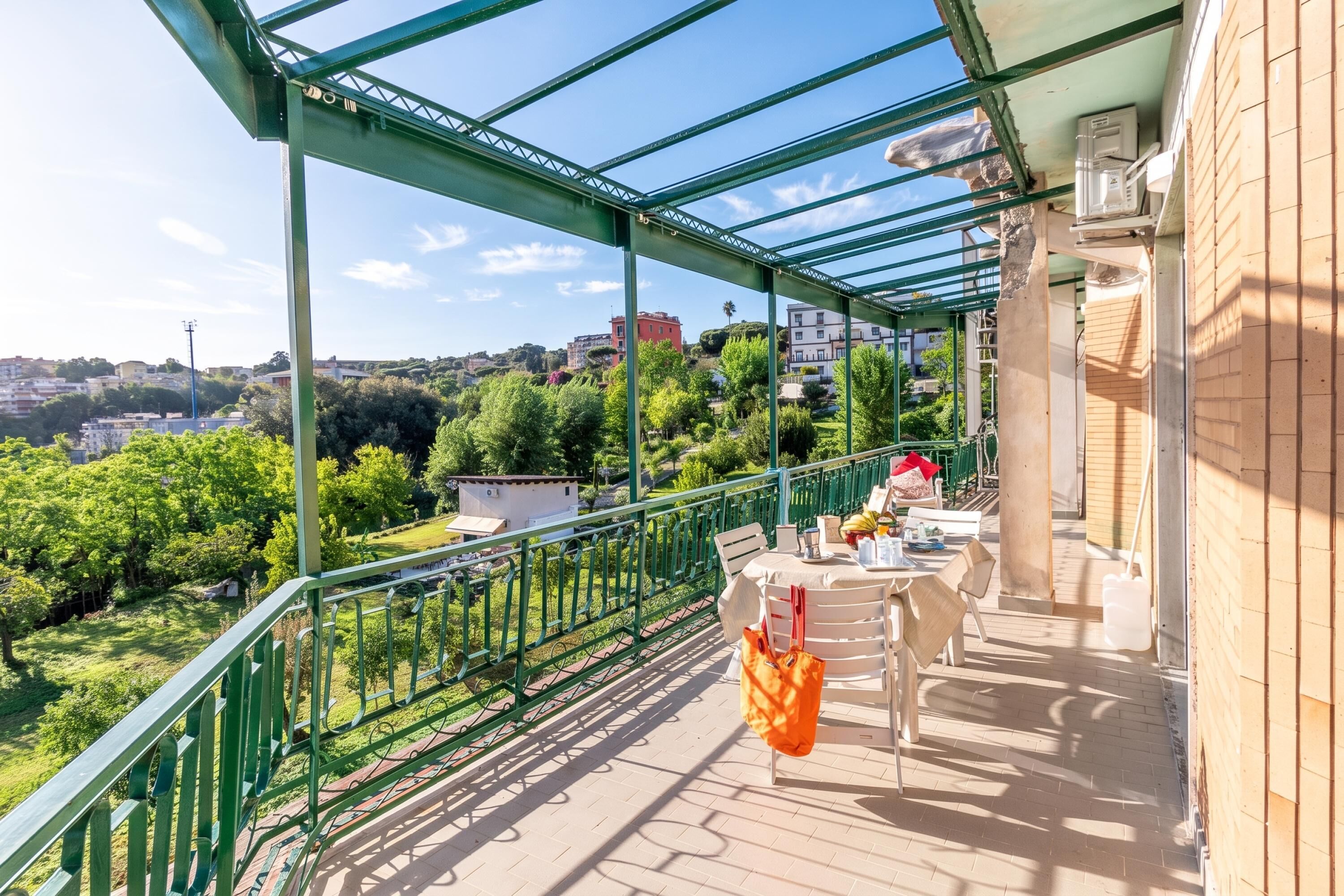 Ein Balkon mit Tisch und Stühlen, der auf einen Stadtblick mit Grünflächen und Gebäuden blickt.