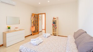 Une chambre à coucher comprenant un lit, une commode, un miroir, une armoire et une porte donnant sur une autre pièce.