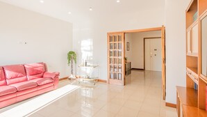 Un salon spacieux avec un canapé rose, une table basse en verre et un meuble en bois.