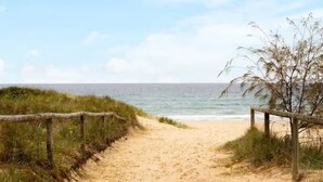En sti langs en sandstrand med trægelændere på hver side, der fører til havet.