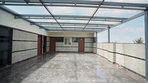 A covered outdoor area with a tiled floor, metal beams, and a door with a window. - The Ekah Comforts  (Bengaluru)