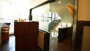 A modern interior with a wooden reception desk, a glass partition, and a staircase leading to an upper level. - The Ekah Comforts  (Bengaluru)