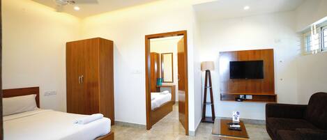 A hotel room with a bed, wardrobe, desk, TV, and a sofa.