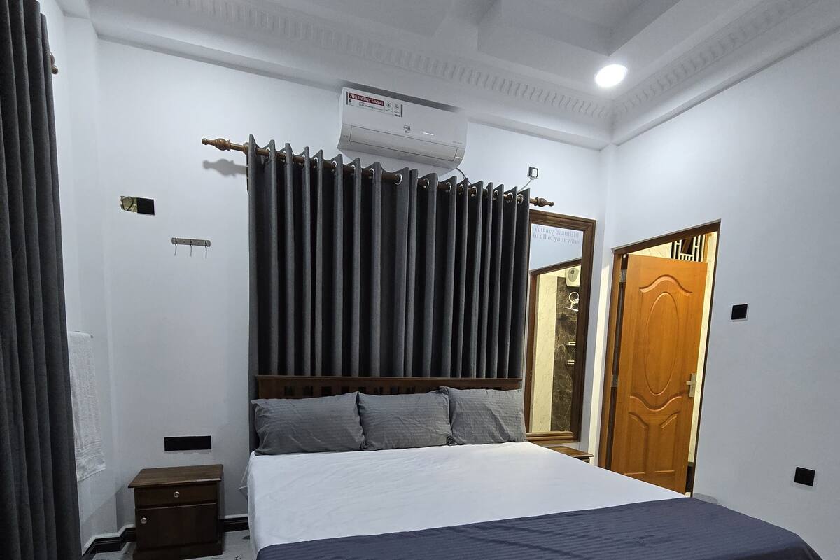 A bedroom with a bed, a nightstand, a wooden door, and a ceiling fan.
