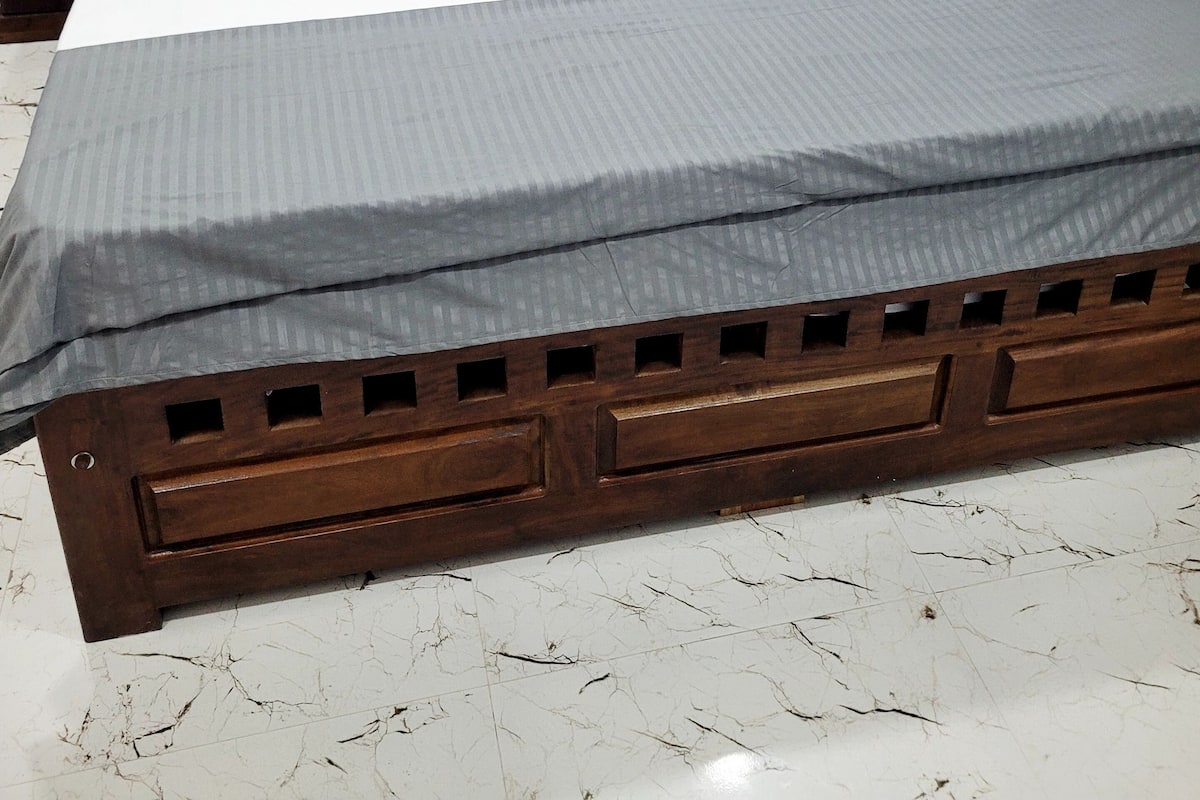 A bed with a wooden frame, grey bedding, and a marble floor.