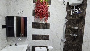 A modern bathroom with a white sink, toilet, and shower. There is a decorative plant on the wall and a mirror above the sink. - Munril Guest (Jaffna)