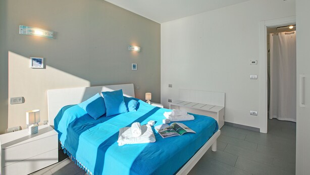 A modern hotel room with a large bed, bedside tables, and a bathroom door. - Sogno Sul Lago, Lakefront Balcony (Laveno Mombello)