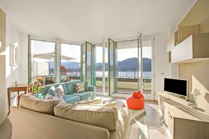 A modern living room with a sofa, a red bean bag, a flat-screen TV, and a balcony with a view.