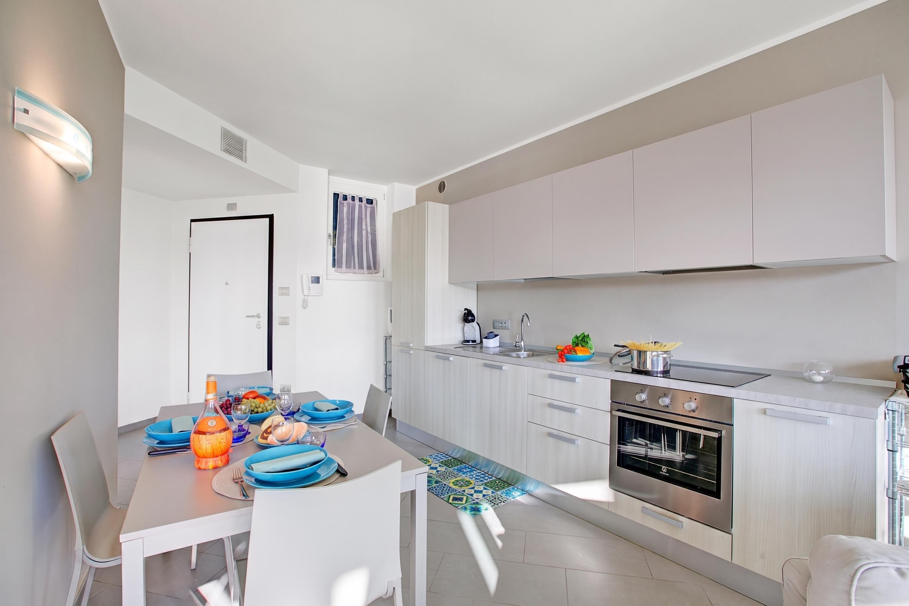 A modern kitchen with a dining area, featuring a built-in oven, a sink, and a dining table set with plates and glasses.