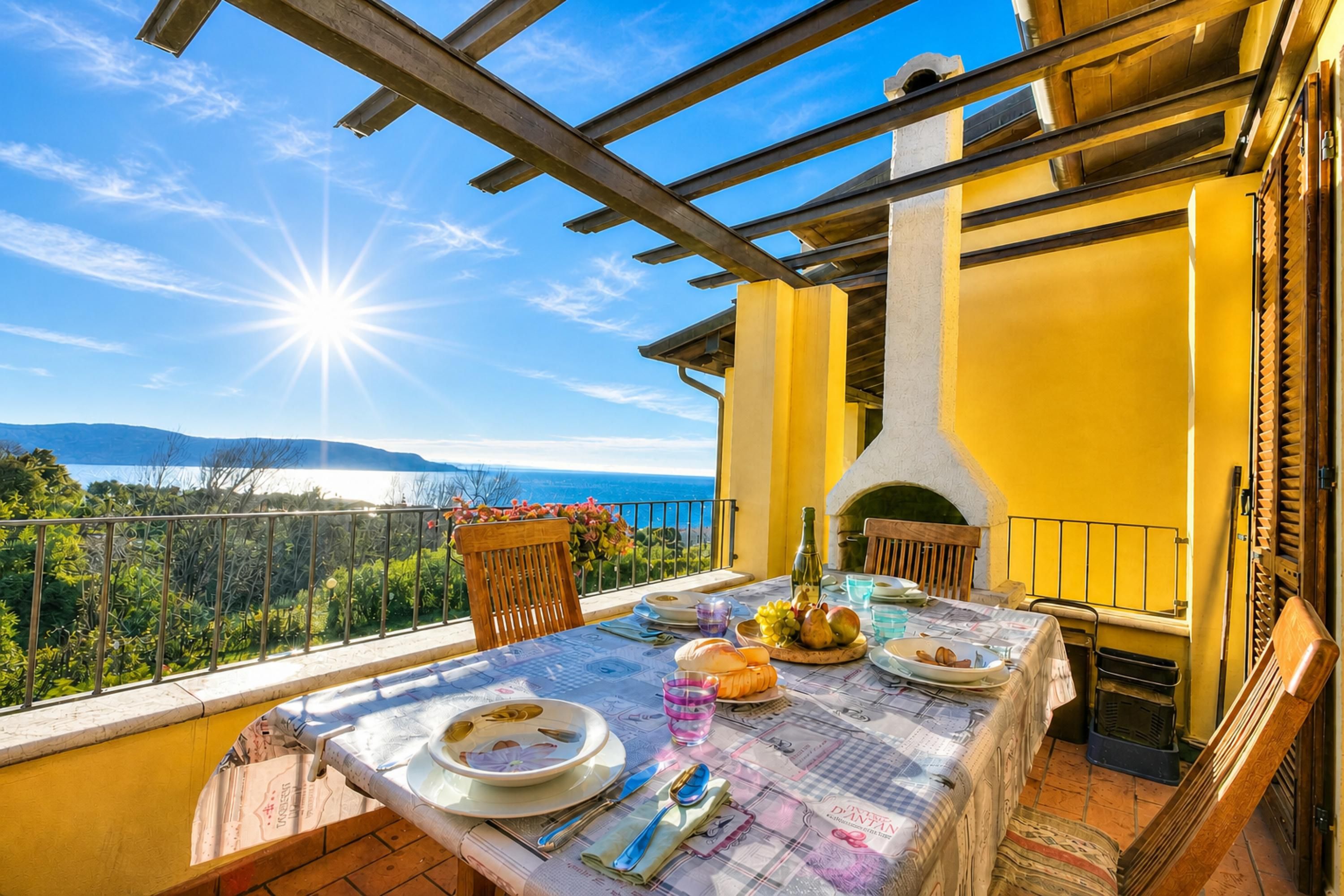 Un balcón con mesa lista para comer, con vistas a un paisaje pintoresco que incluye montañas y una masa de agua.