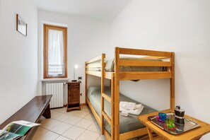 A bunk bed with a wooden frame, a desk with a chair, a radiator, a window with a curtain, and a tray with a kettle and cups. - Julia's House With Lakeview and shared pool (Toscolano Maderno)