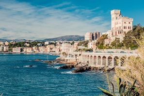 A coastal town with a prominent castle-like building, a bridge, and a rocky shoreline. - House Rondinella Genova City Center (Genoa)