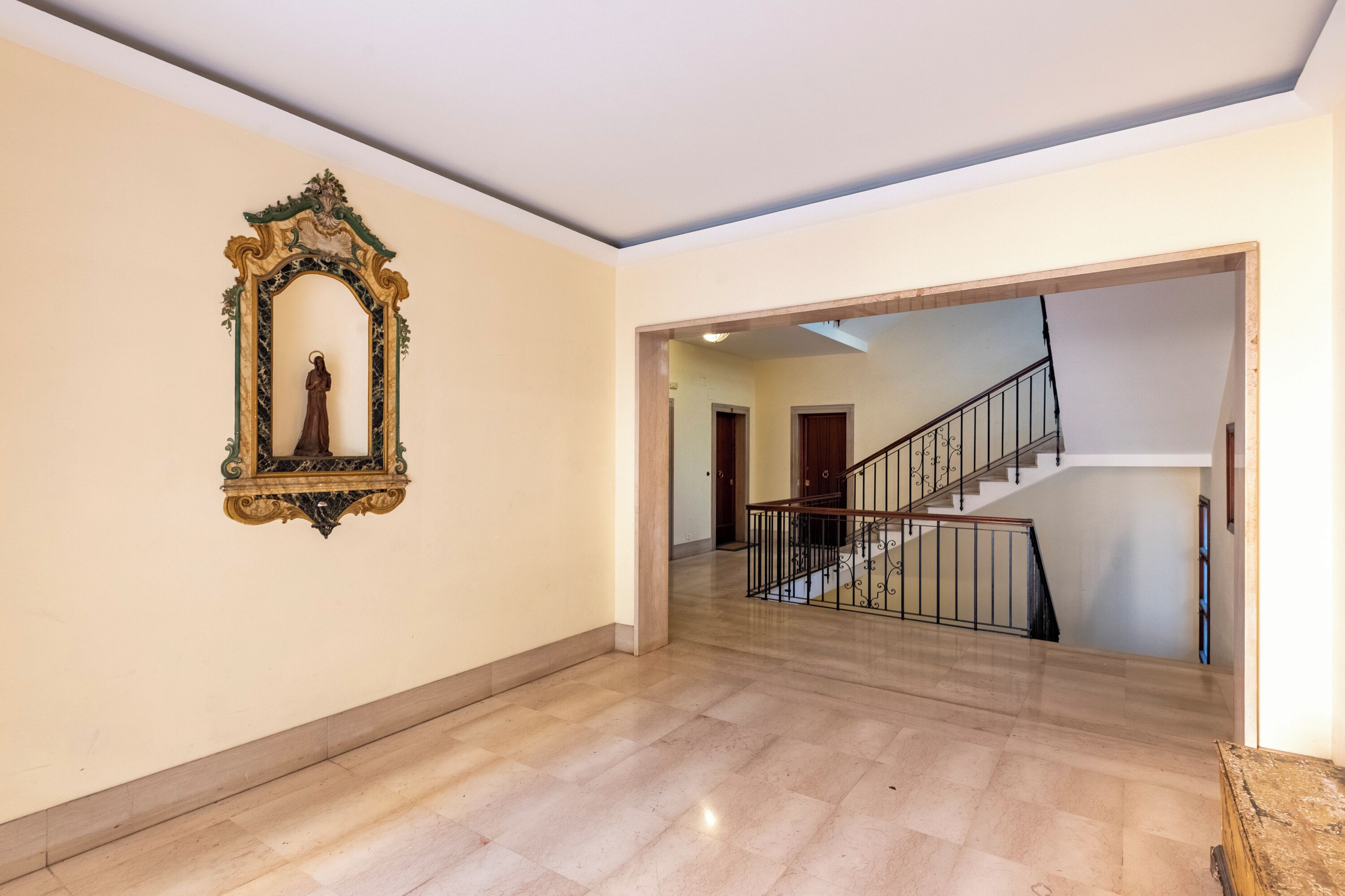 A spacious hallway with a marble floor leading to a staircase with a metal railing.