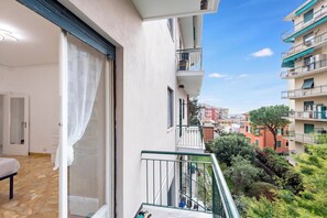 A balcony with a view of a cityscape, a door with a curtain, and a small table with a chair. - House Rondinella Genova City Center (Genoa)