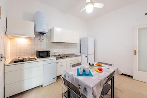 A compact kitchen with white cabinets, a microwave, a sink, and a dining area with a table set for two. - House Rondinella Genova City Center (Genoa)