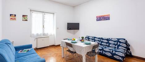 Cozy living space with a dining area, featuring a sofa, dining table, and flat-screen TV.