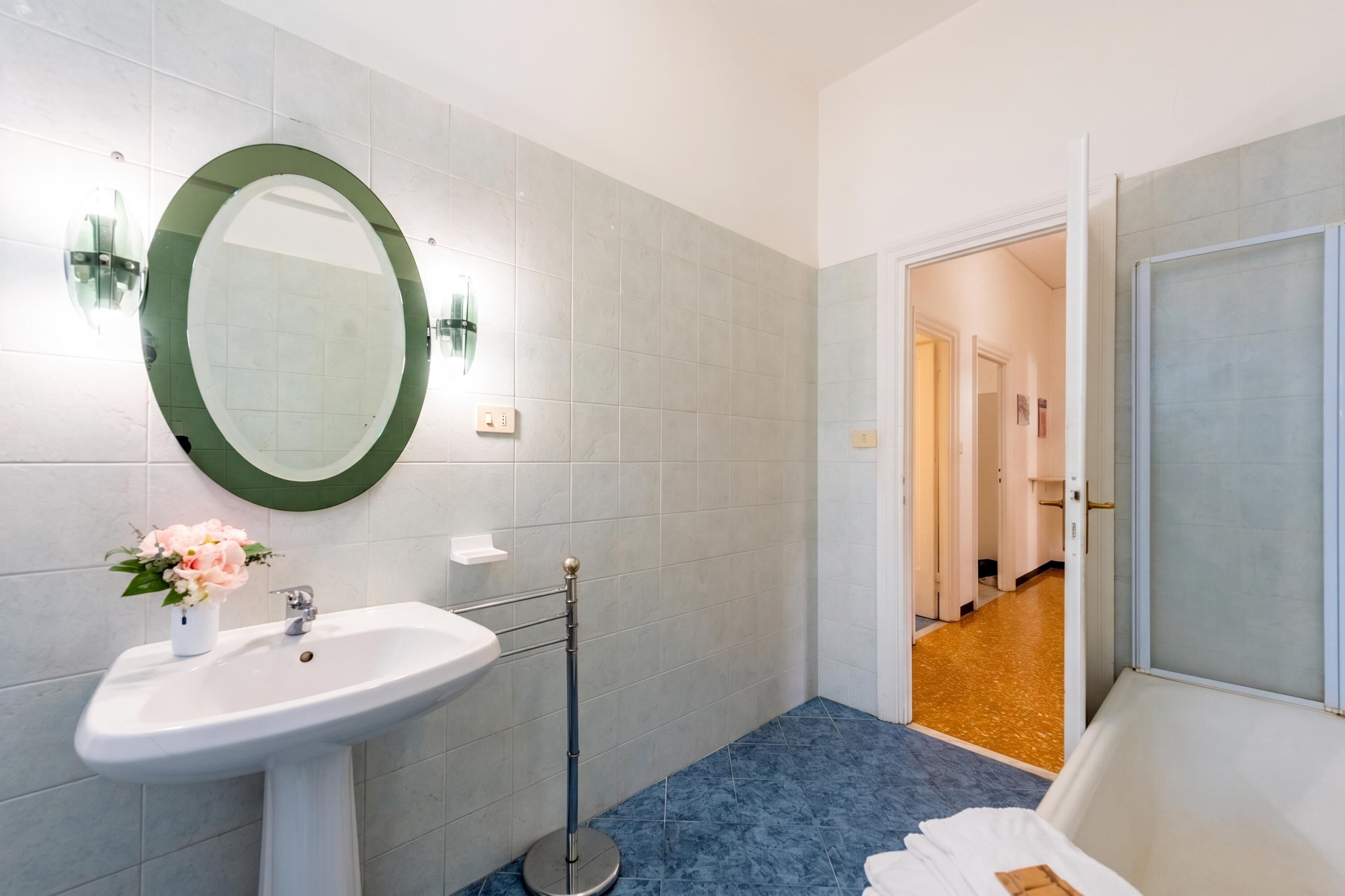 Een badkamer met een witte wastafel, een ronde spiegel en een blauwe vloer.