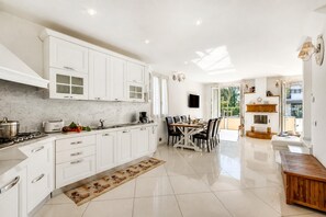 Une cuisine moderne avec des meubles blancs, un coin repas doté d’une table et de chaises en bois, et une vue sur l’extérieur grâce à de grandes fenêtres.