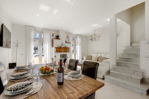 A dining area with a wooden table set for four, a bottle of wine, and a fruit bowl. There is a staircase leading to another level.
