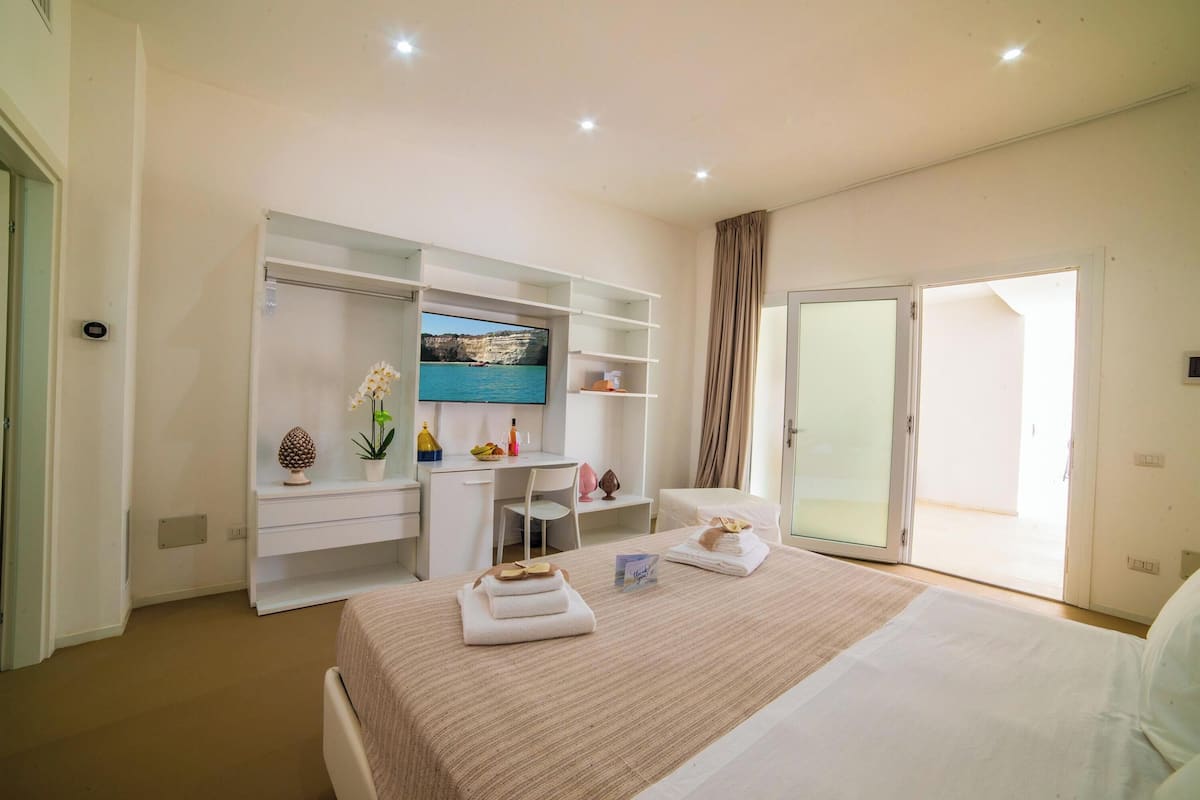 A hotel room with a bed, a desk, a TV, and a sliding glass door to the outside.