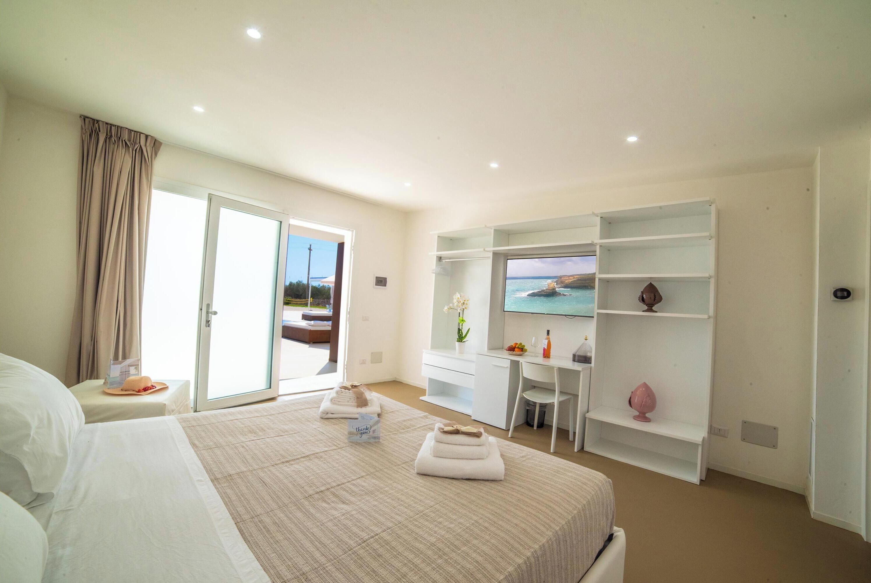 A hotel room with a bed, a desk, a chair, a TV, and a balcony with a view.