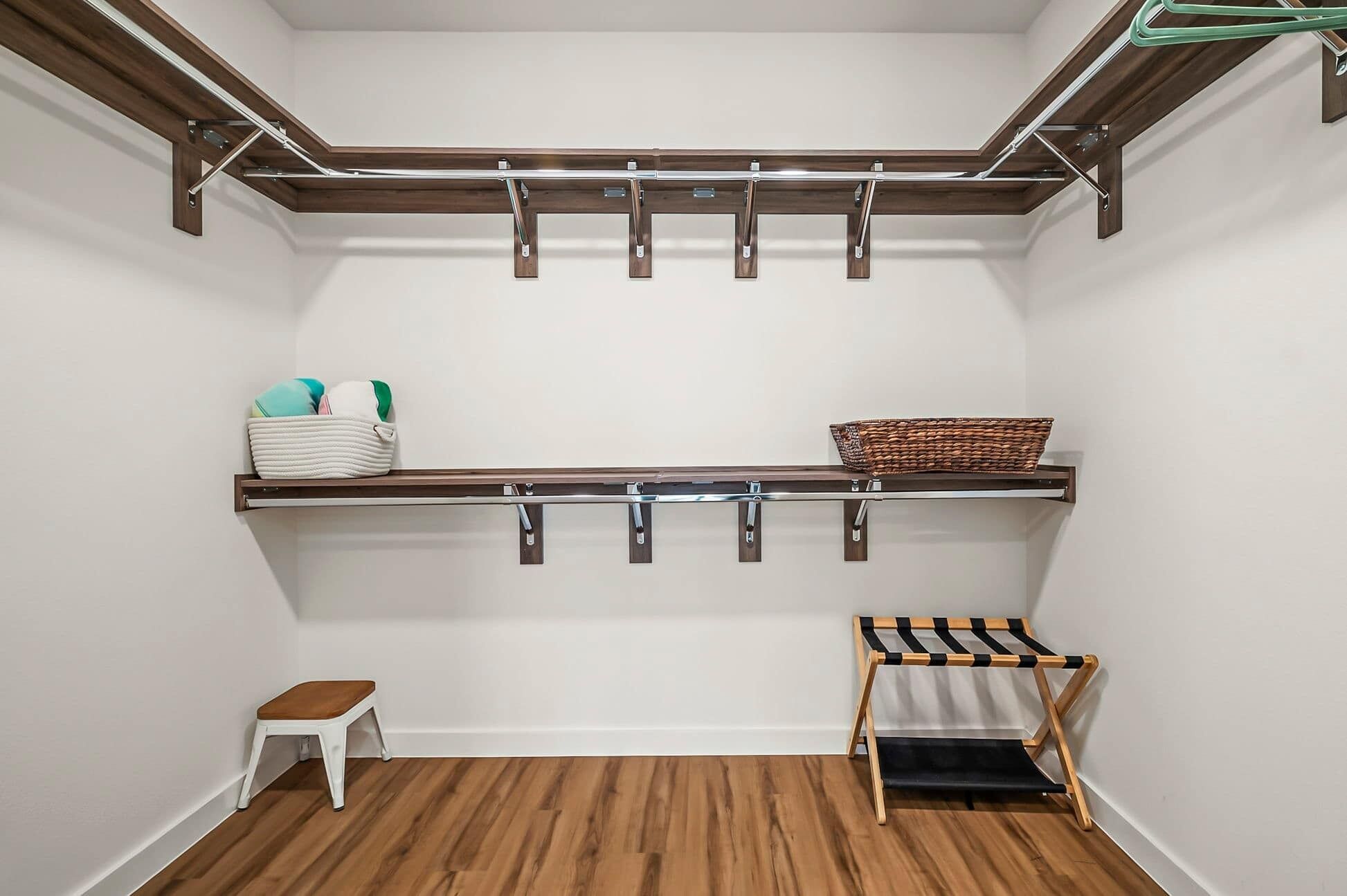 Un vestidor con suelo de madera, un banco, una percha y estantes con ropa doblada y una cesta.