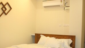Una cama bien hecha en una habitación de hotel, con cabecera de madera, unidad de aire acondicionado montada en la pared y ventilador de techo.