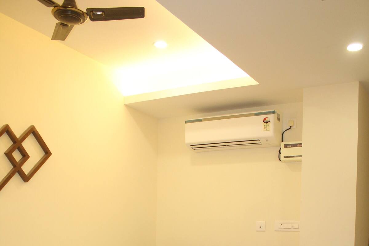 A neatly made bed in a hotel room with a wooden headboard, an air conditioning unit mounted on the wall, and a ceiling fan.