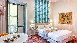 A hotel room with a bed, bedside lamps, a table with a tray, a window with a view, and a wall with a striped pattern and artwork.