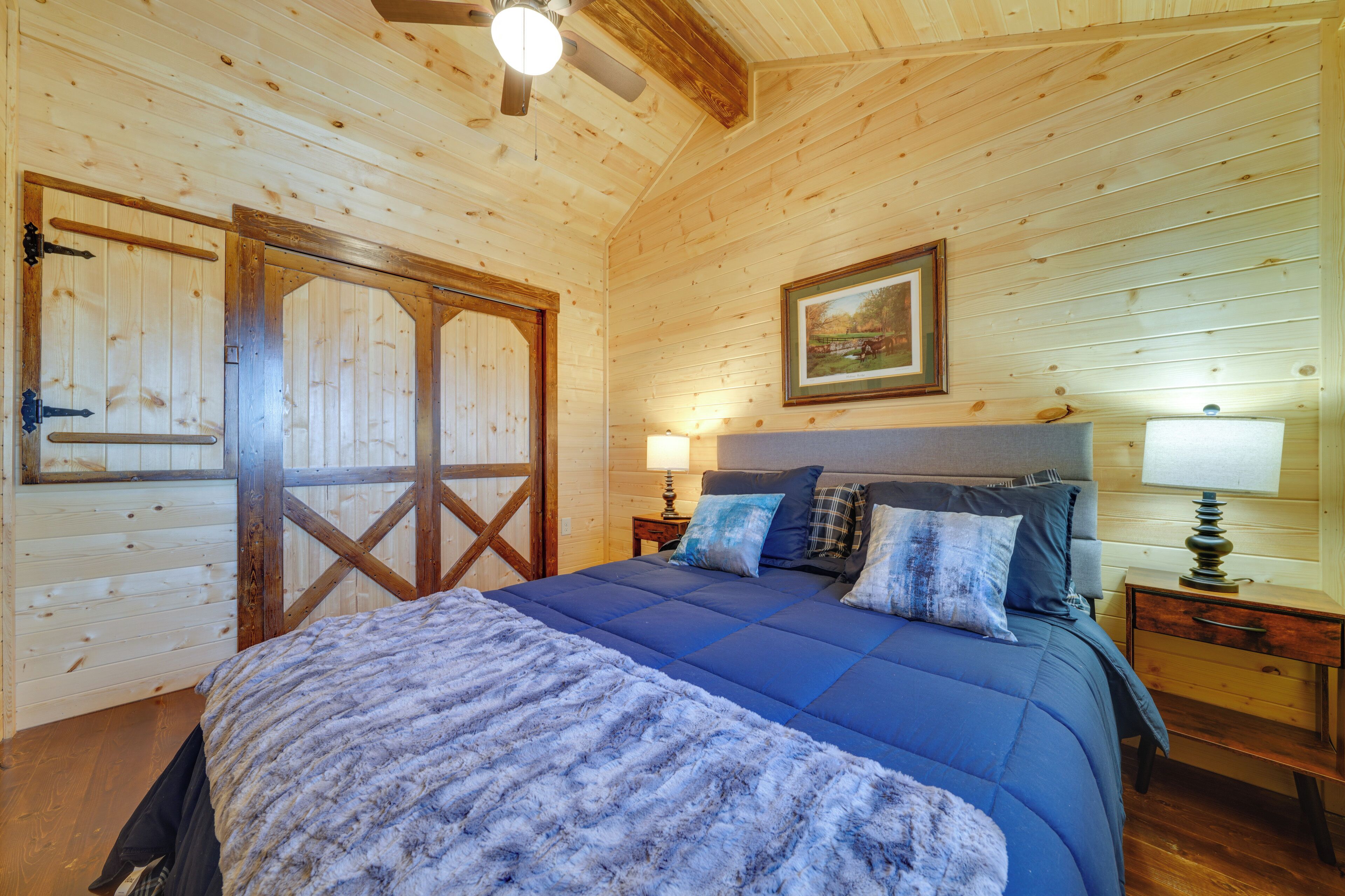 Camera da letto in una baita di legno con un letto, un comodino, una lampada e una ventola a soffitto.