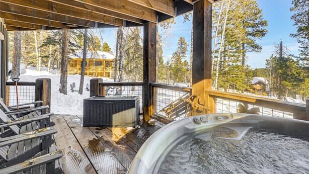 A wooden deck with a hot tub, outdoor seating, and a view of a snowy landscape with trees and a building in the background. - Black Hills Cabin w/ Hot Tub! 20 Mi to Sturgis (Lead)