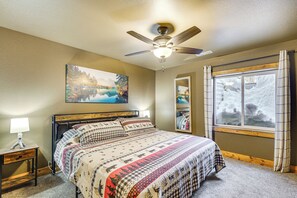 A bedroom with a bed, a ceiling fan, a nightstand with a lamp, a window with curtains, and a painting on the wall. - Black Hills Cabin w/ Hot Tub! 20 Mi to Sturgis (Lead)