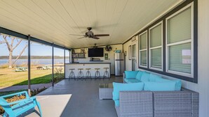 A covered porch with a ceiling fan, outdoor seating, a kitchen area, and large windows overlooking a grassy area. - Dock & Patio: Possum Kingdom Lake House (Graford)