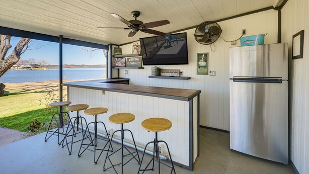 A kitchen with a bar area, a refrigerator, a television, and a view of the lake. - Dock & Patio: Possum Kingdom Lake House (Graford)