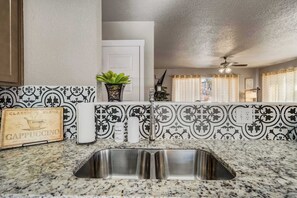 A kitchen with a stainless steel sink, patterned backsplash, and a ceiling fan.