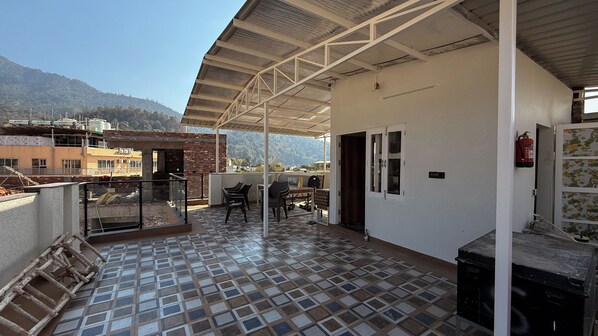 Un balcón techado con suelo de baldosas, una mesa con sillas y vistas de los edificios y colinas circundantes.