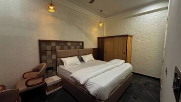 Una habitación de hotel con cama, sillón, armario y dos lámparas de pared.