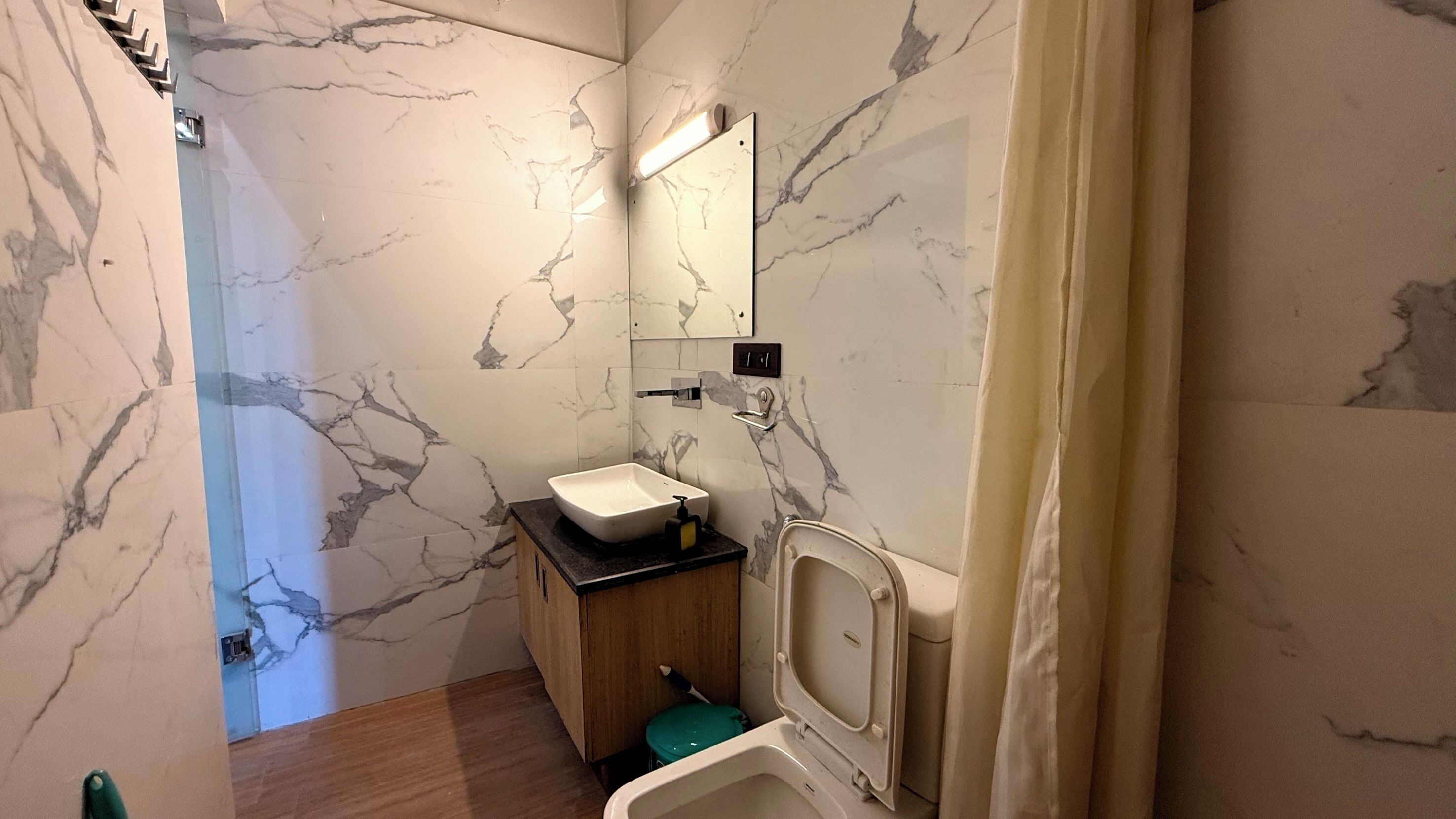 A bathroom with marble walls, a white sink, a mirror, and a toilet.