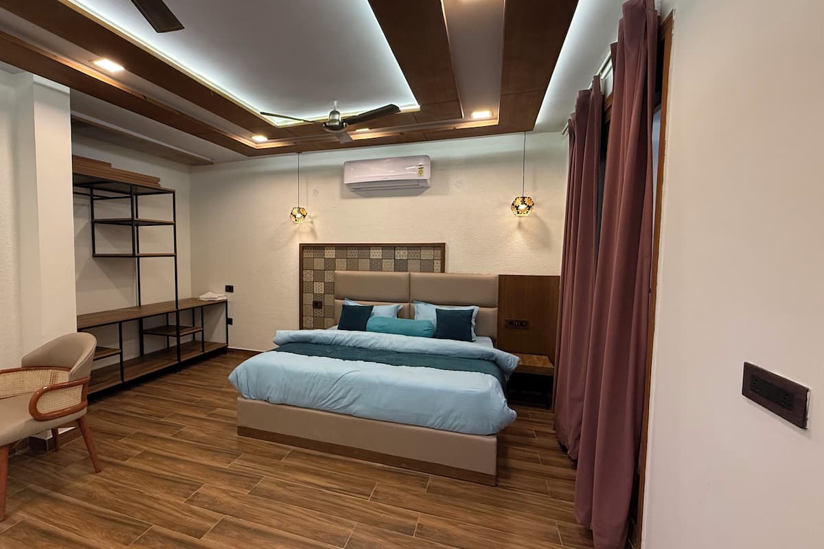 A modern bedroom with a bed, a chair, a small table, a ceiling fan, and an air conditioning unit.