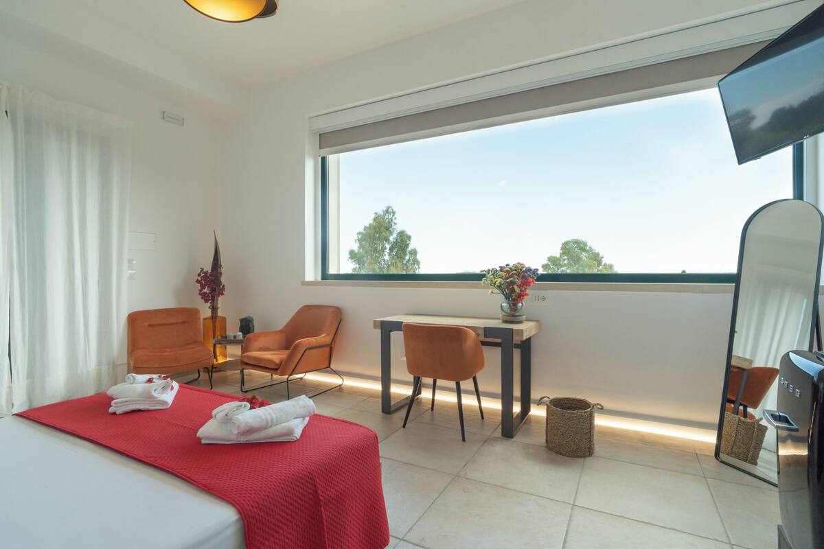 Une chambre d’hôtel avec un lit, deux chaises, une table et une grande fenêtre.
