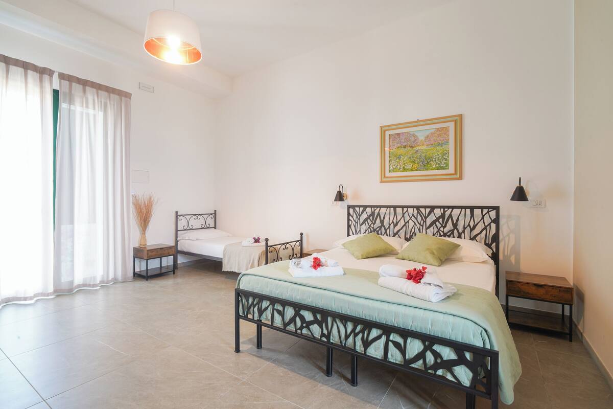 Une chambre à coucher avec un grand lit, un lit plus petit, une table de chevet, une lampe et un tableau au mur.