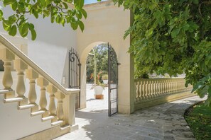 Un escalier en pierre mène à une entrée en arc surmontée d’un portail en fer forgé.