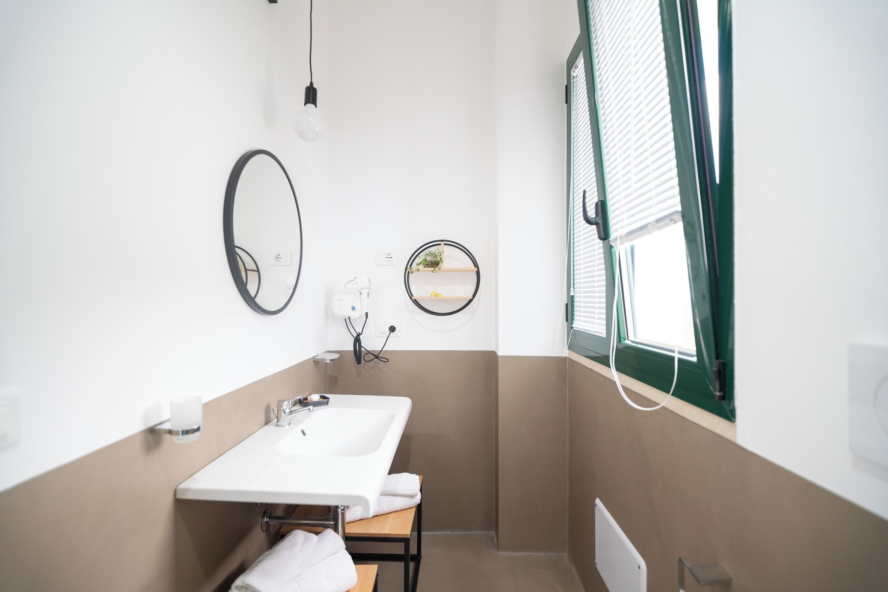 A small bathroom with a white sink, two mirrors, a towel rack, and a window with blinds.
