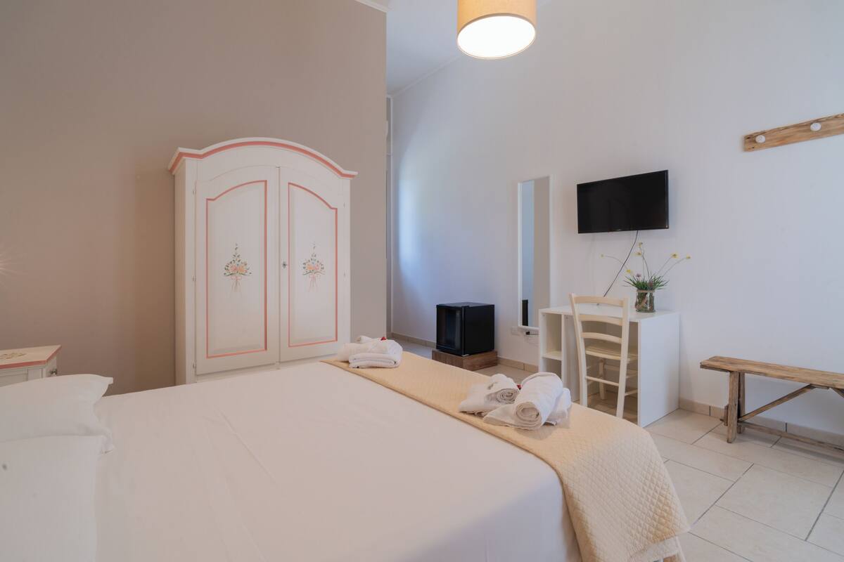 Une chambre d’hôtel comprenant un lit, une armoire, un téléviseur, un bureau avec une chaise et un banc.