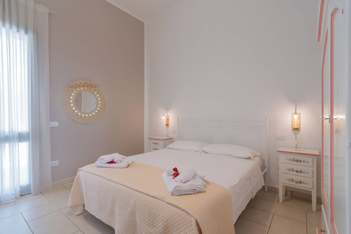 Une chambre bien rangée, avec un lit, des tables de chevet, un miroir et une fenêtre avec des rideaux.