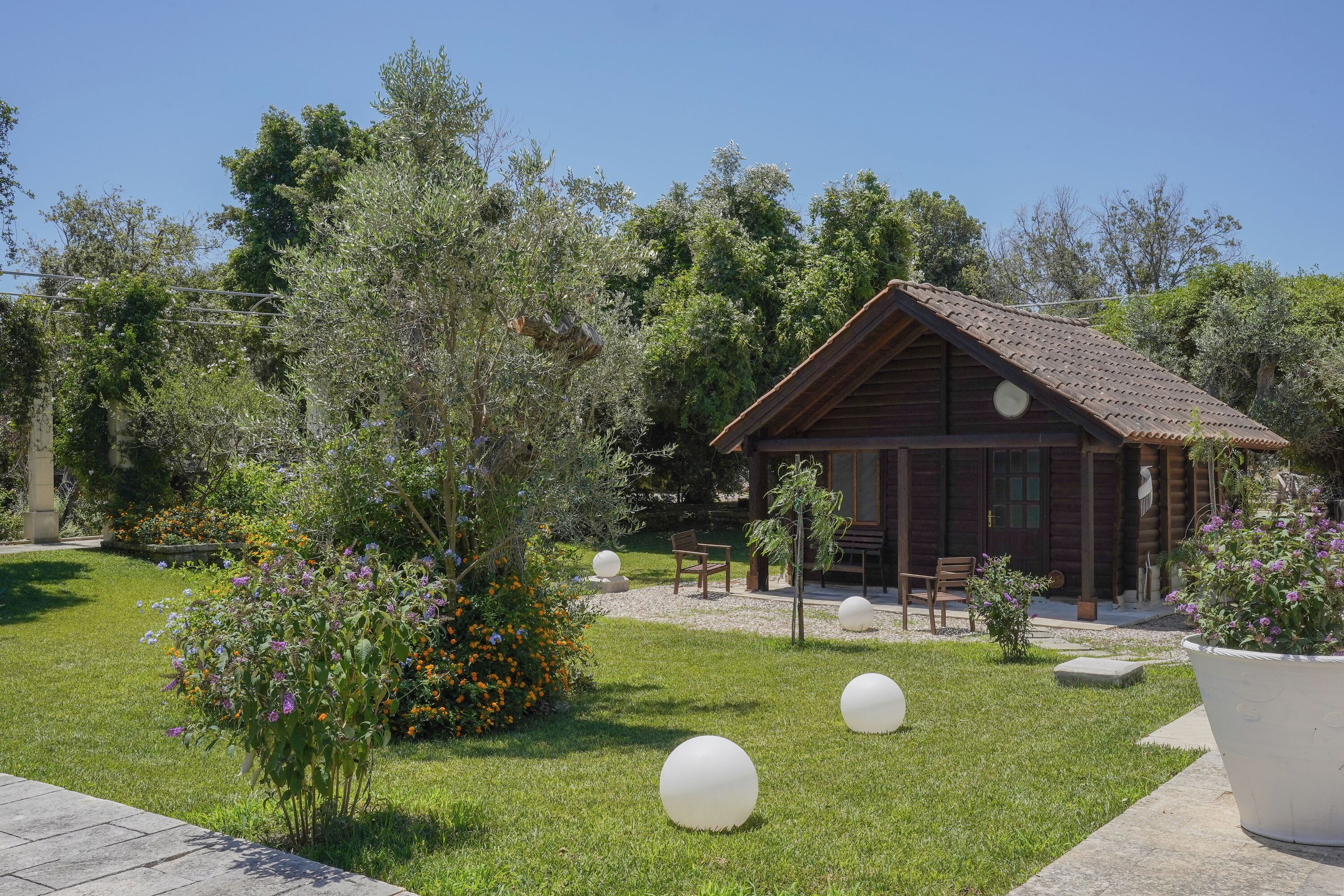 A rustic cabin with a tiled roof, surrounded by a well-maintained lawn and flowering plants.