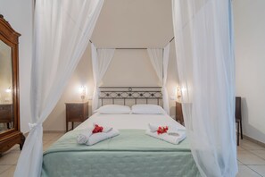 Un lit à baldaquin avec des rideaux blancs, une couvre-lit verte et des serviettes ornées de fleurs rouges.
